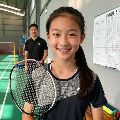 15岁学员王悦的肖像照,扎着马尾辫,手持羽毛球拍微笑站在伟德体育场馆内,身后是她的私教教练和训练计划白板。